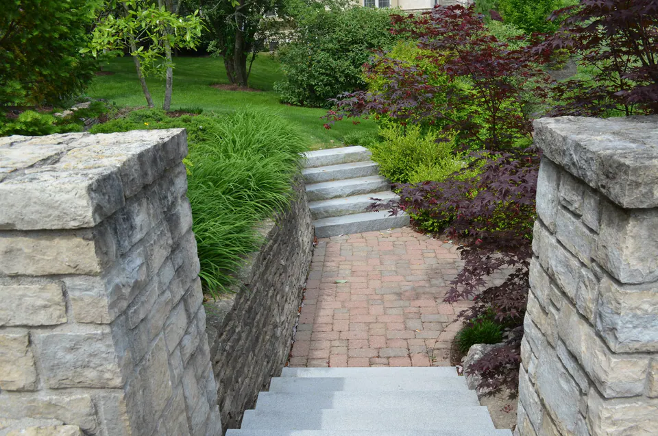 Cut stone piers and walls framing a brick walk and granite steps up a garden slope